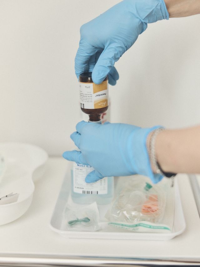 Hände in Handschuhen halten ein braunes Glasfläschchen über einer Schale